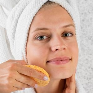 Žena sa peškirom na glavi čisti lice sunđerom kao pripremu kože pre faceliftinga - Plastične operacije u Turskoj